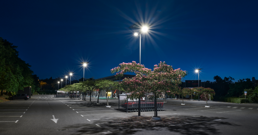 Solar-powered streetlights illuminating a parking lot with blooming crepe myrtle trees at dusk in South Carolina.