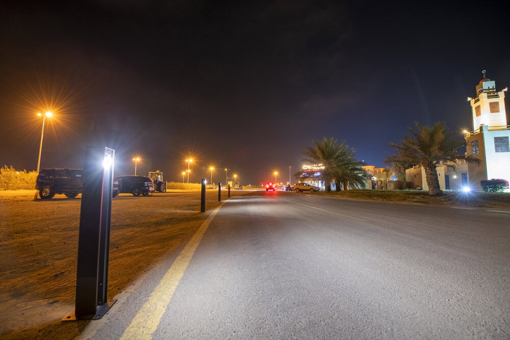 Solar bollard lights installed along a roadway and parking area at night, improving safety, visibility, and resilience with off-grid illumination.