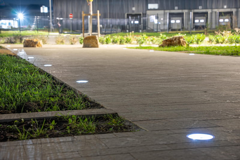 High-performance solar lights for commercial parking lots, providing sustainable lighting solutions. NOWATT solar architectural lighting integrated into a pedestrian pathway, featuring low-profile illuminated studs for parks, campuses, and landscape environments.