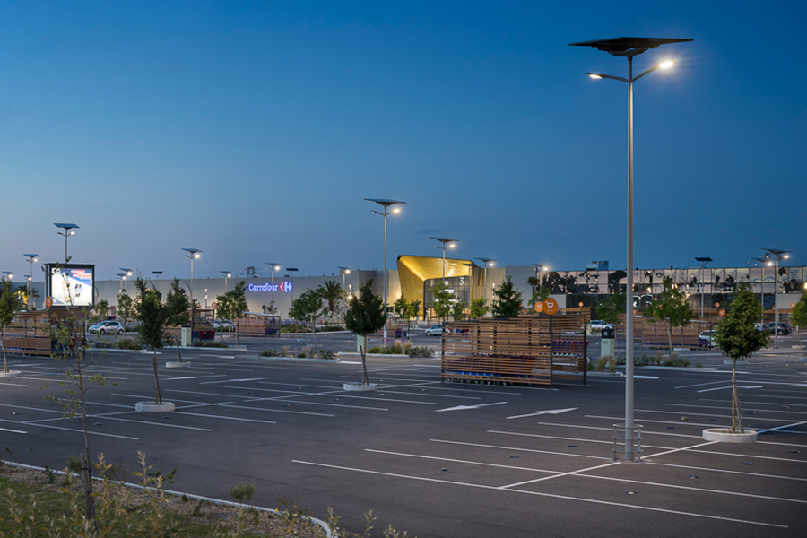 Solar-powered lighting illuminating a retail shopping center parking lot with bright LED fixtures for walkways, storefront access, and customer safety at night.
