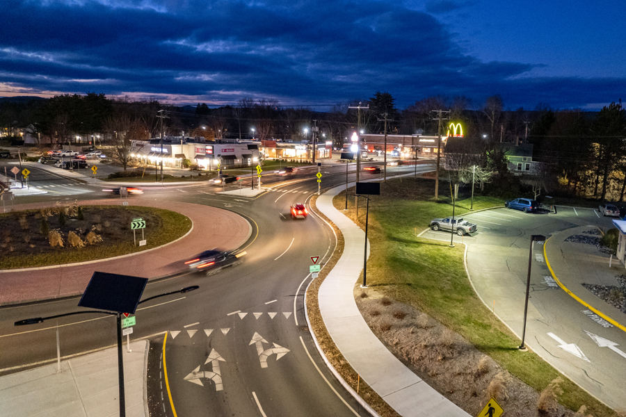 Aerial view of a well-lit roundabout at dusk with off-grid solar streetlights illuminating sidewalks and roadways, reducing it's carbon footprint