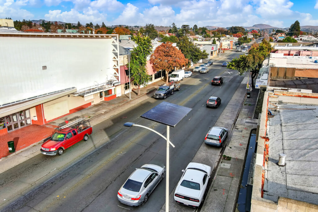 Solar-powered streetlight on a busy downtown street in Vallejo, California, with vehicles, storefronts, and urban infrastructure in view.