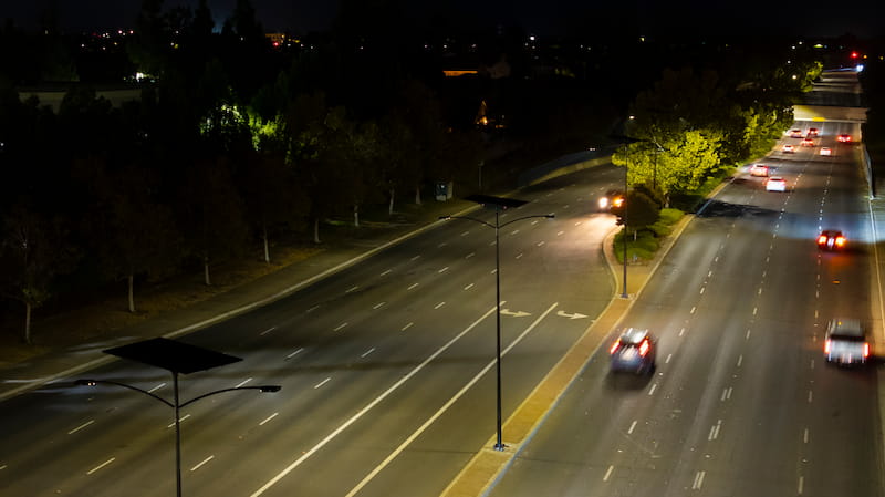 Solar-powered streetlights line a multi-lane residential arterial road at night, protecting the night sky and community safety 
