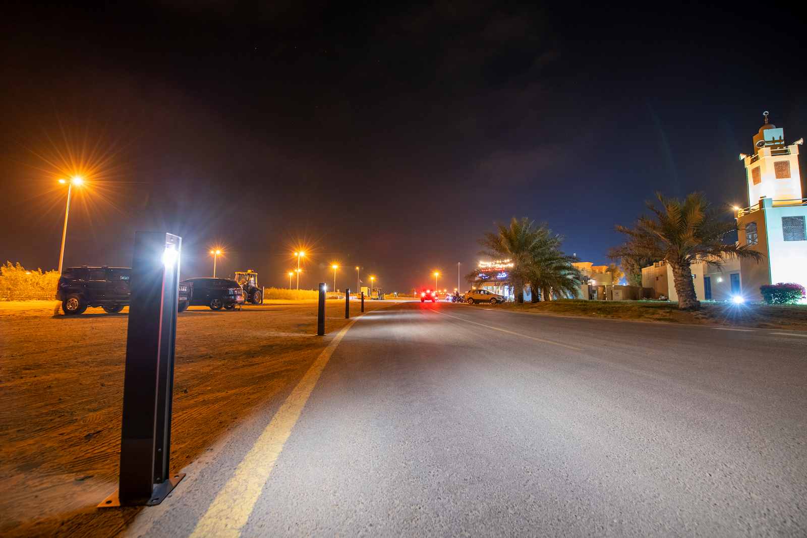 Durable solar bollard lights illuminating a roadway and parking lot perimeter at night, improving visibility, safety, and resilience with off-grid lighting.