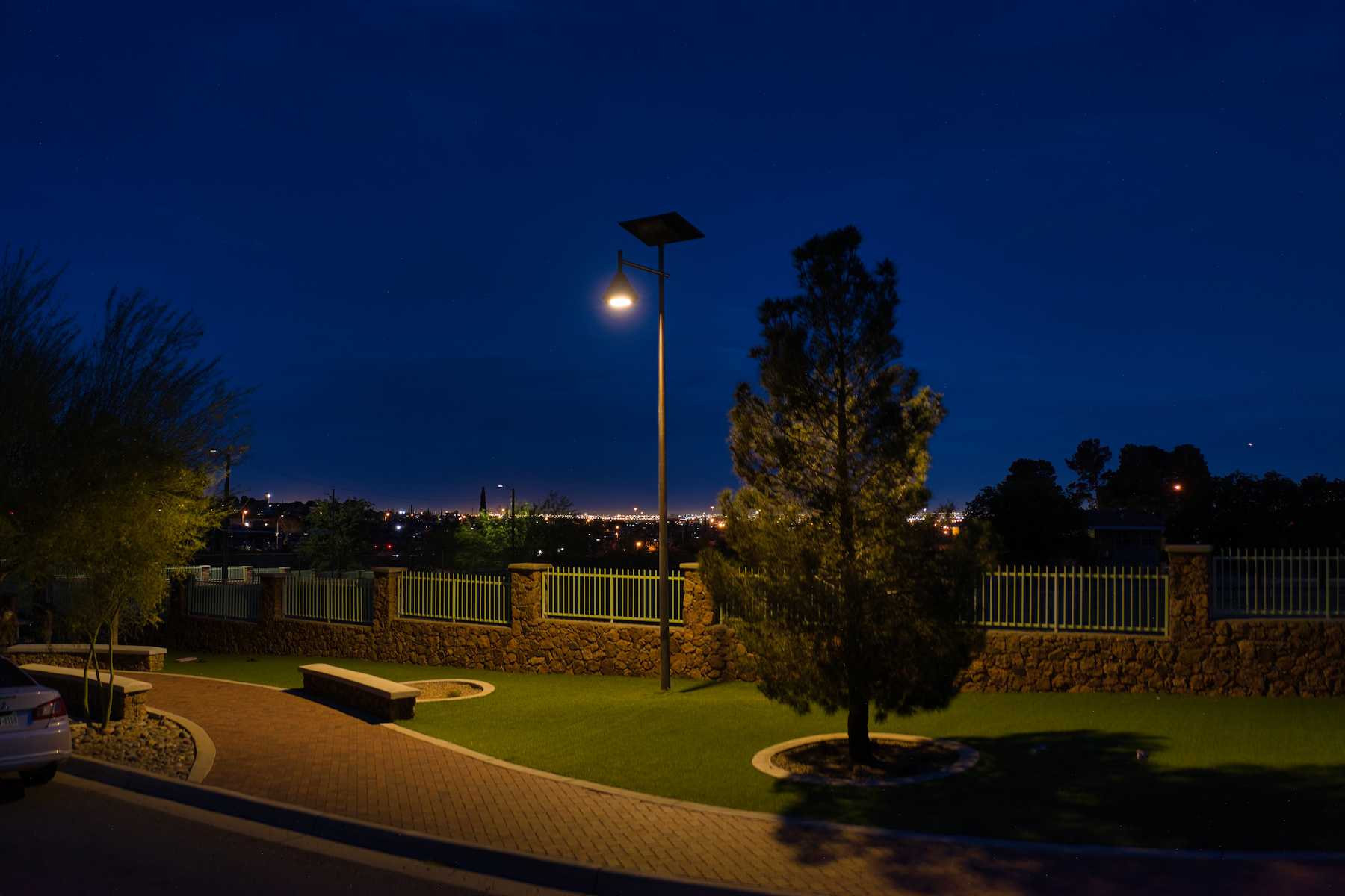 Solar-powered streetlight illuminating a landscaped park area with stone fencing, overlooking a city skyline at night in South Carolina.