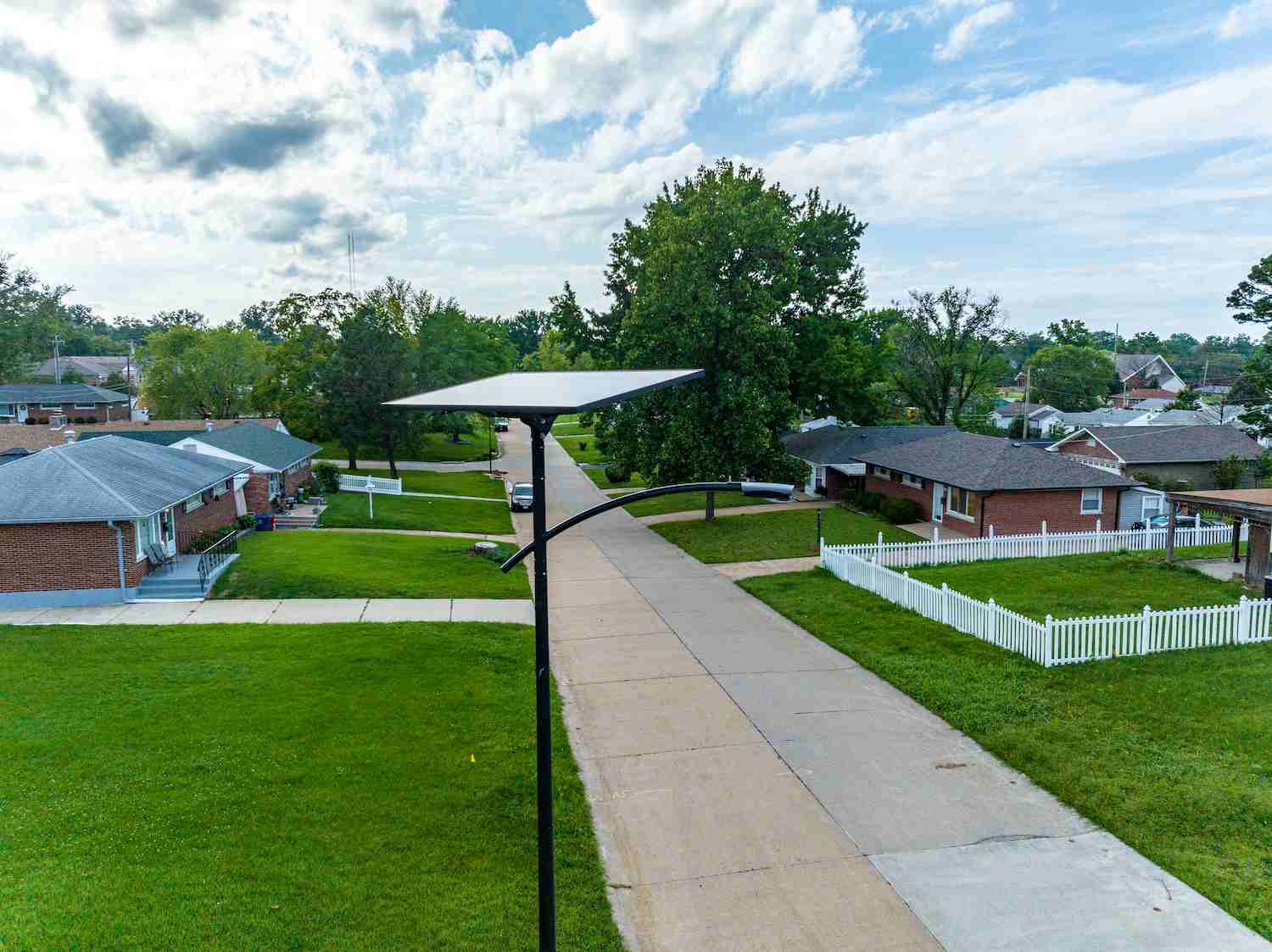 Fonroche solar streetlight illuminating a quiet residential neighborhood in Georgia with green lawns, sidewalks, and single-family homes — no wires or trenching visible.