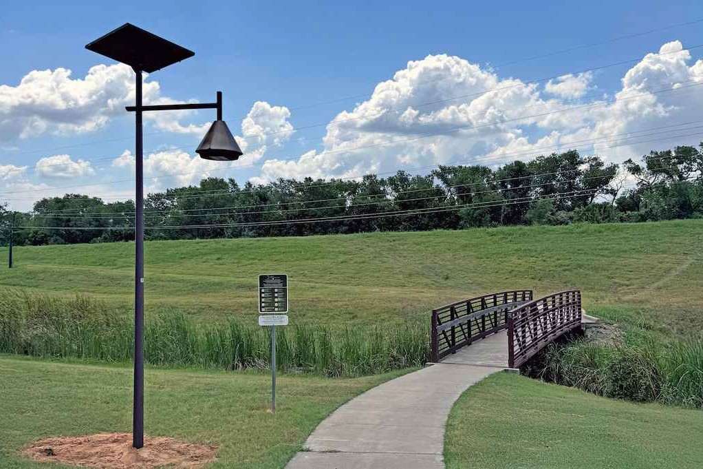 Solar-powered streetlight illuminating a walking path and pedestrian bridge in a Georgia park, showcasing sustainable lighting for public green spaces.