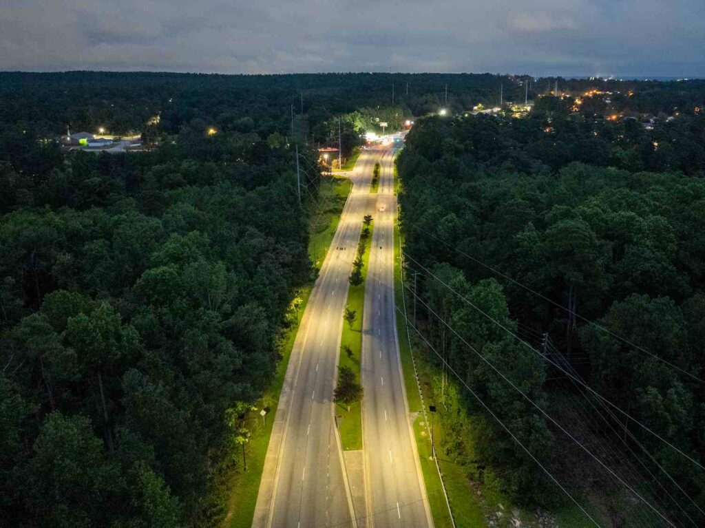 Aerial view of solar-powered streetlights illuminating a Georgia highway through a forested corridor, providing safe, off-grid lighting at night.