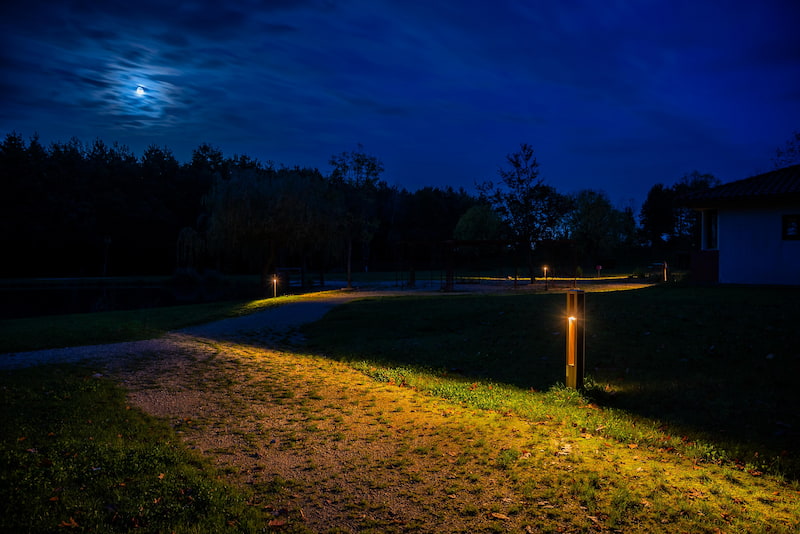 Nowatt solar bollard pathway lights illuminating a park trail at night with warm, low-impact lighting under a moonlit sky