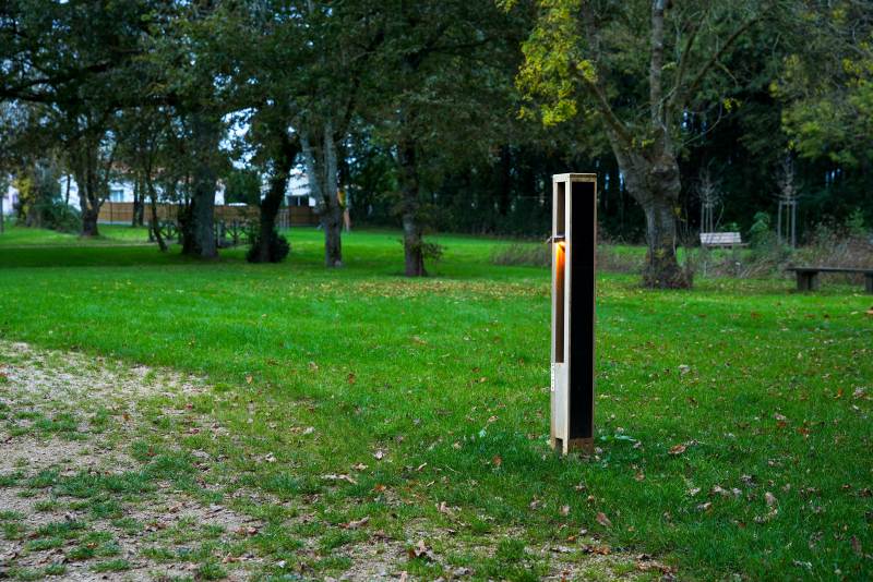ADA-compliant solar bollard providing off-grid pathway lighting in a green park setting surrounded by trees.