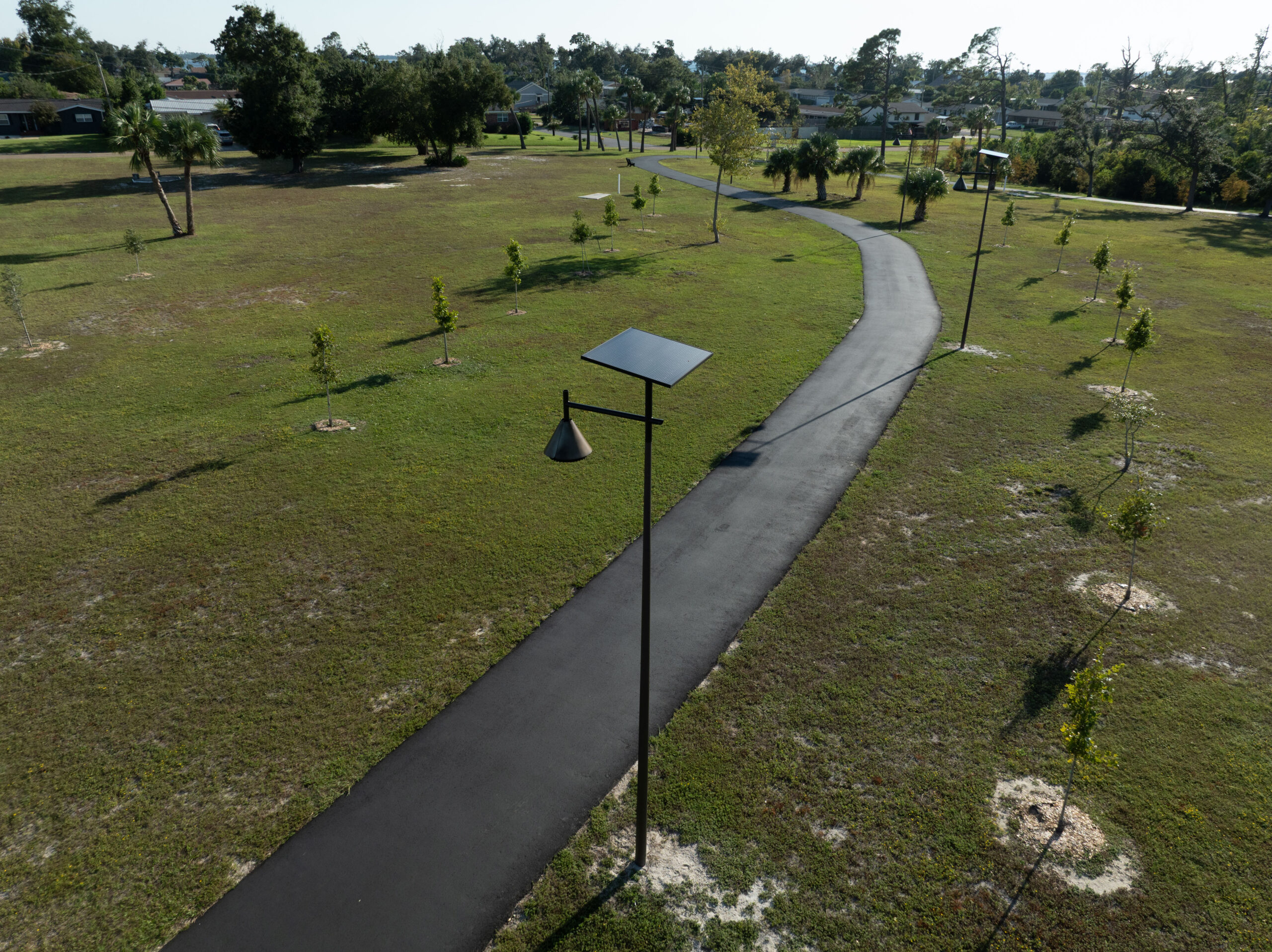SmartLight-park-pathway-overview Solar-powered landscape lighting illuminating a paved walking trail through a residential park with off-grid pathway lights for parks, greenways, and HOA communities.