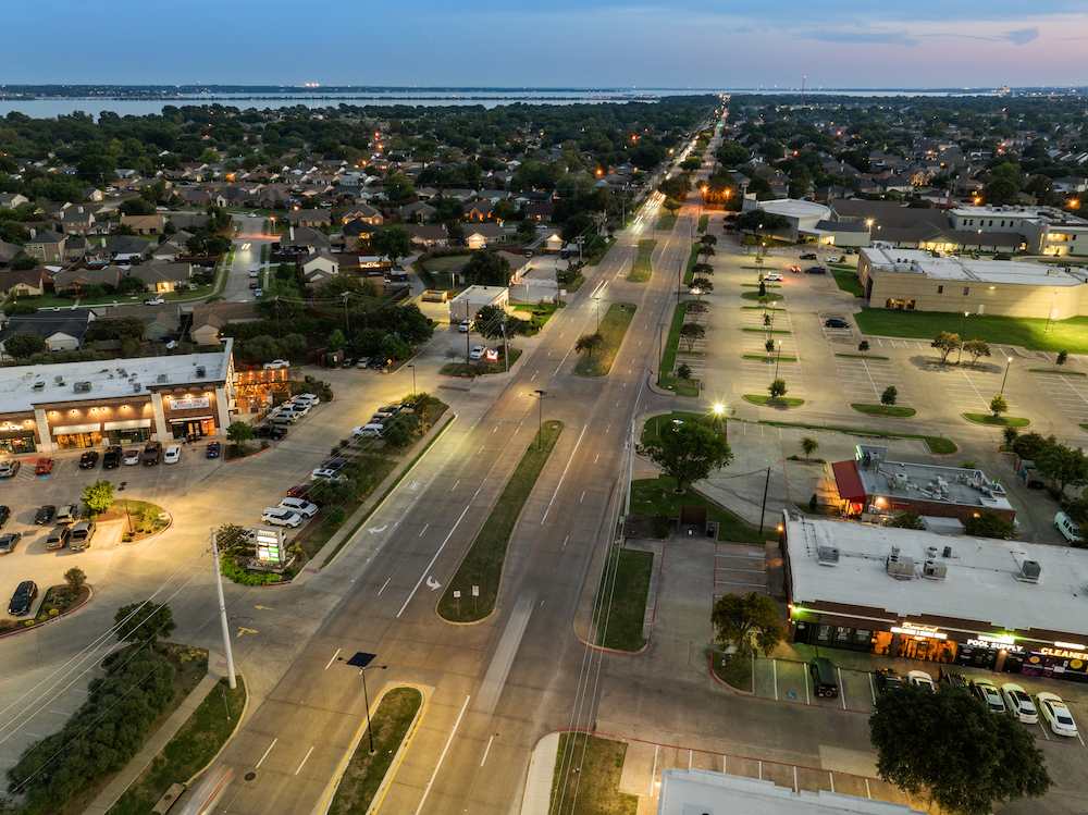 Aerial view of a well-lit commercial and residential corridor in Rowlett, Texas, showing solar-powered streetlights along a main road at dusk.