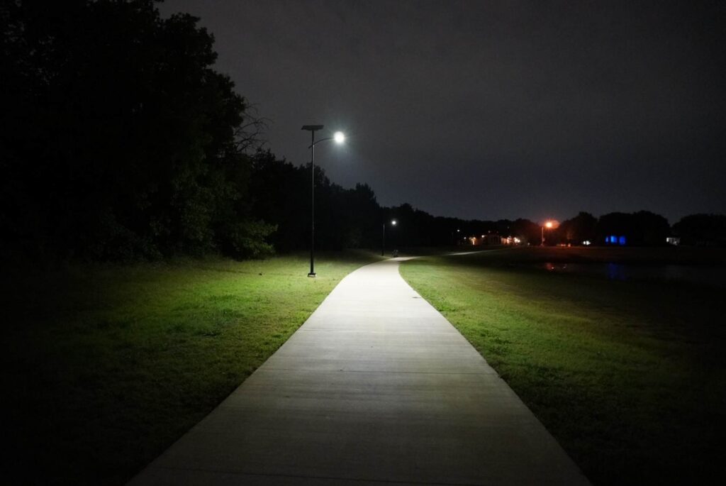 Curved concrete trail illuminated at night by solar-powered streetlights, enhancing safety and visibility in a greenway park.