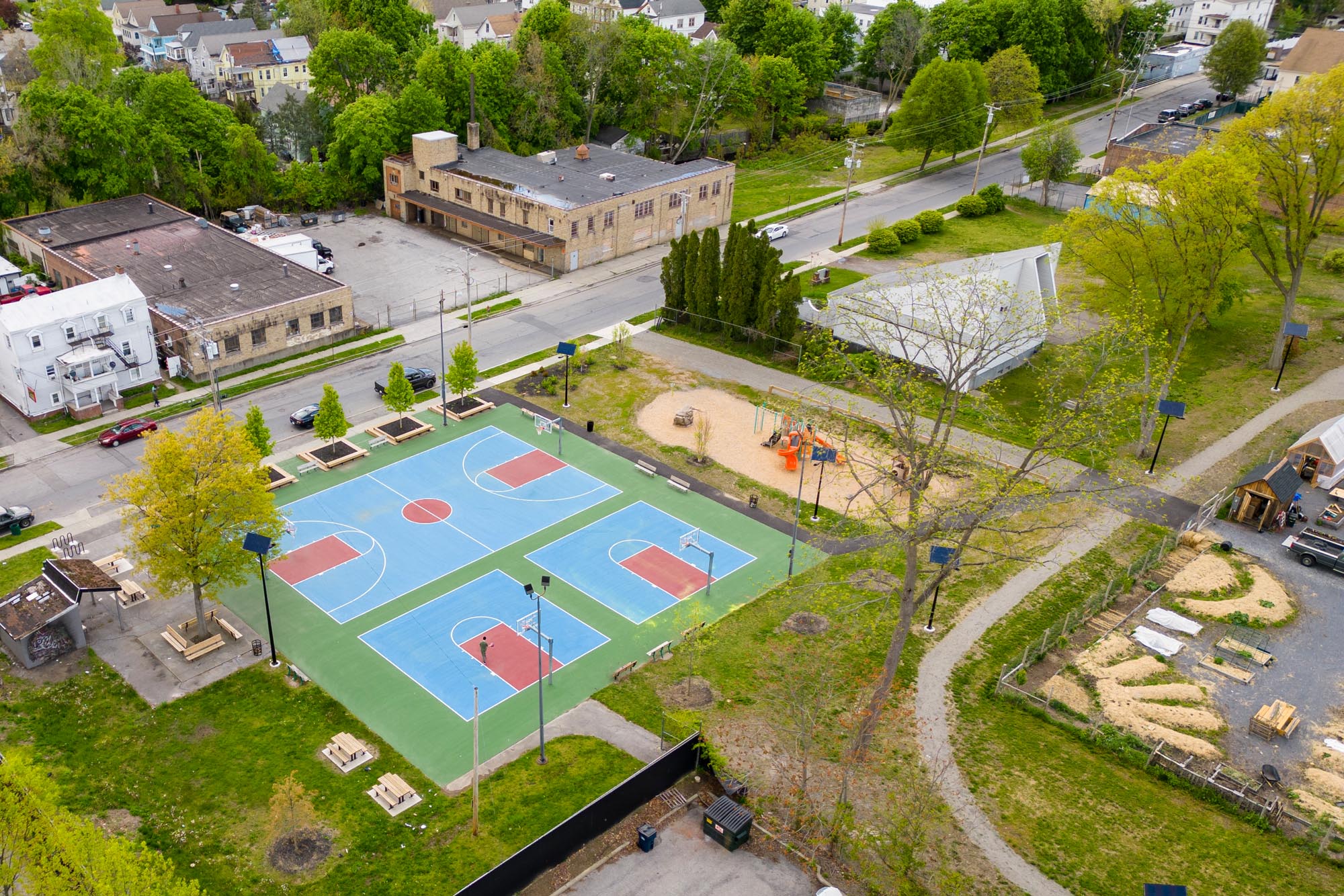 Aerial view of a public park with solar-lit basketball courts, playground, walking paths, and community garden.