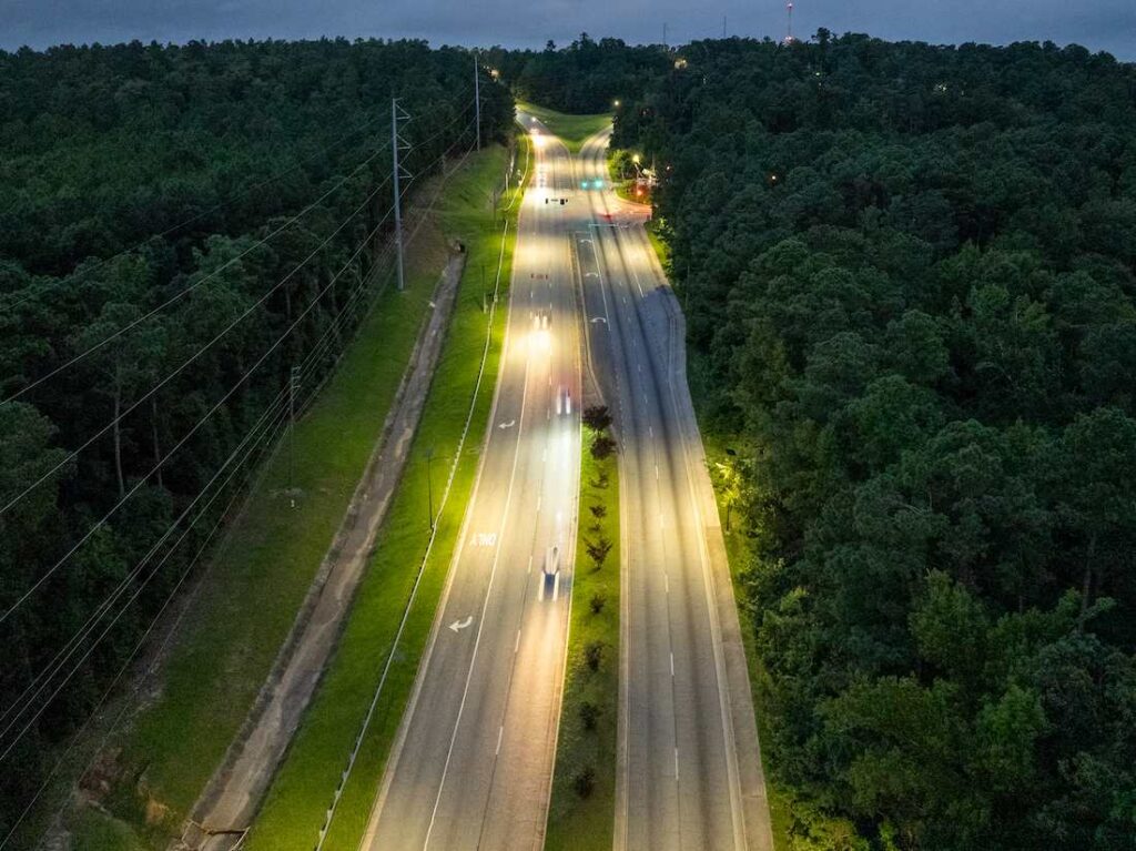 Aerial view of off-grid solar streetlights illuminating a Georgia highway during stormy evening conditions, showing bright and reliable lighting along a tree-lined roadway.