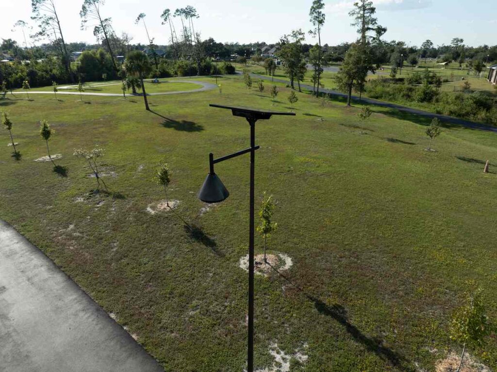 Solar-powered streetlight illuminating a green public park with walking paths and young trees in a suburban South Carolina community.