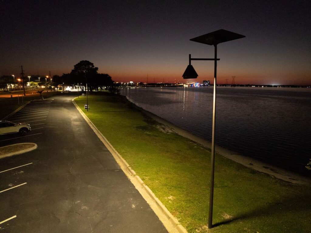 Solar-powered streetlight illuminating a waterfront parking area in South Carolina at dusk, enhancing safety and visibility near public shoreline spaces.