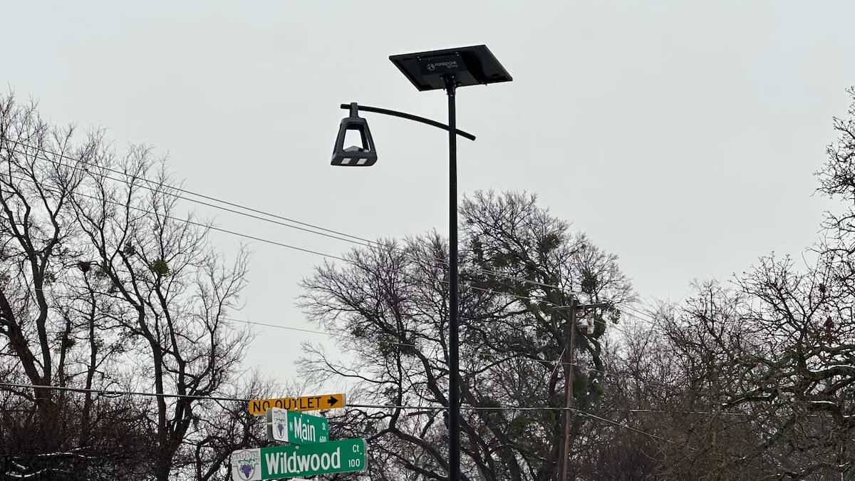 Solar street light at a snowy intersection near Main Street and Wildwood Road, surrounded by winter trees under an overcast sky.