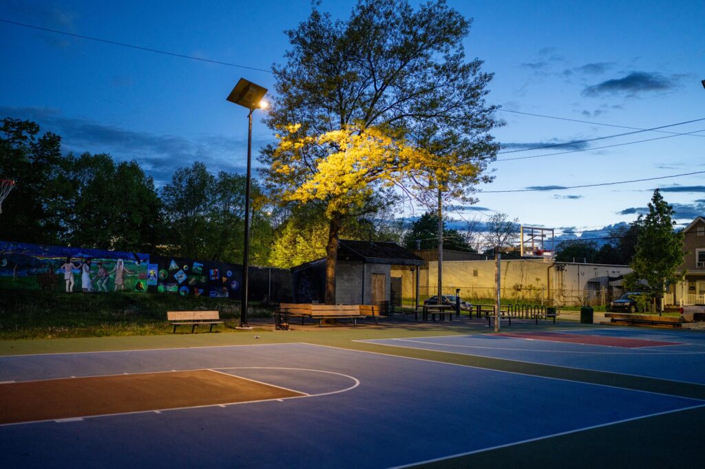 Solar-lit outdoor basketball courts at night, fully illuminated by off-grid lighting systems along benches in a public park.