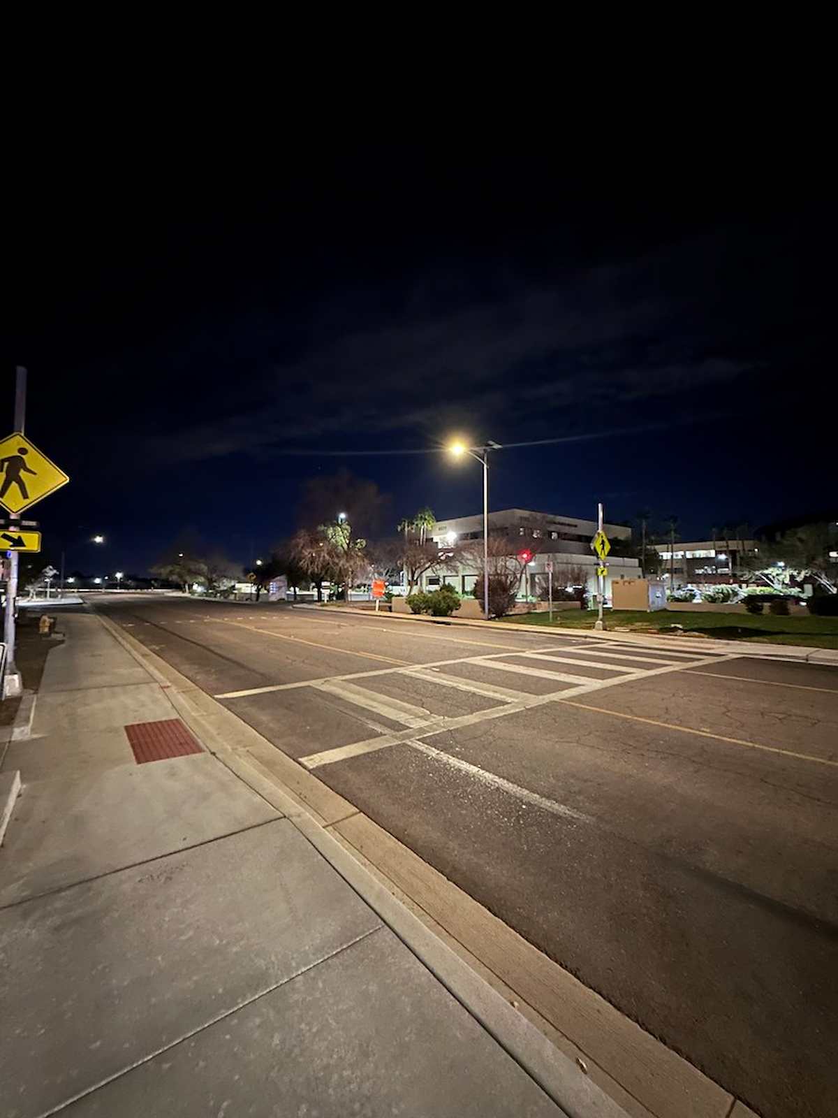 Solar-powered street lighting illuminating a pedestrian crosswalk and sidewalk at night with off-grid lighting designed to improve roadway visibility and pedestrian safety.