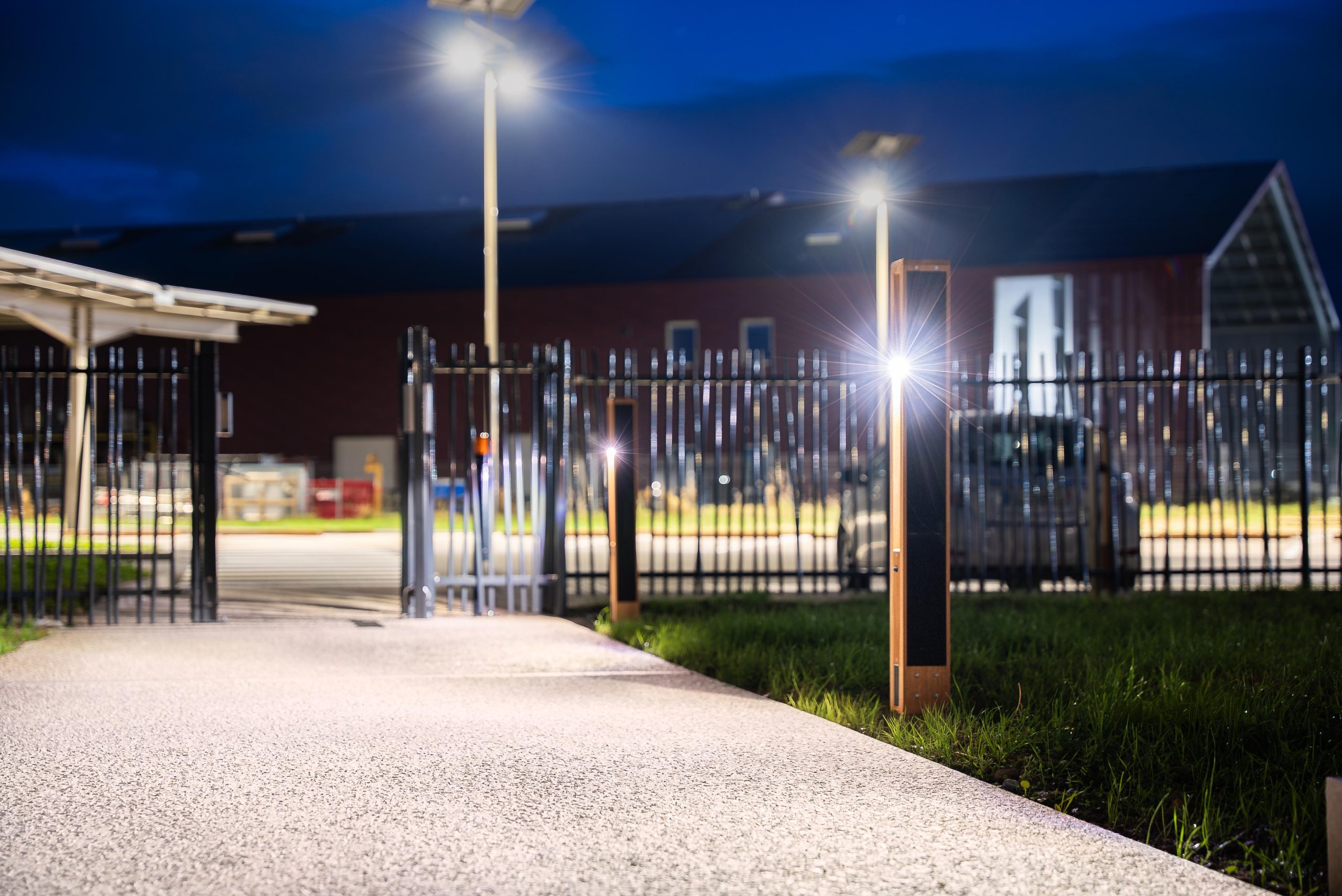 solar-bollard-lighting-commercial-entrance-pathway-night.jpg Smart solar bollard lighting illuminating a pedestrian pathway and park entrance at night with app-controlled architectural outdoor lighting.