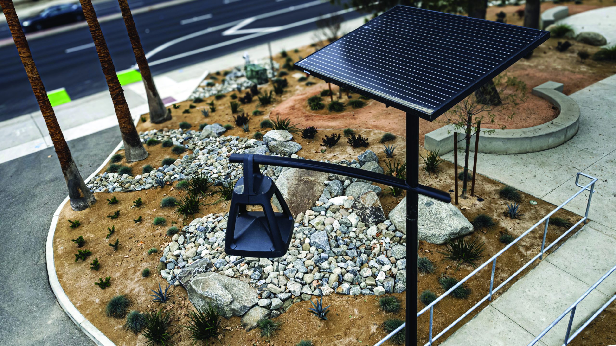 BELLE EPOQUE decorative solar street light with integrated solar panel installed in a landscaped urban streetscape with rocks, pathways, and modern public infrastructure.