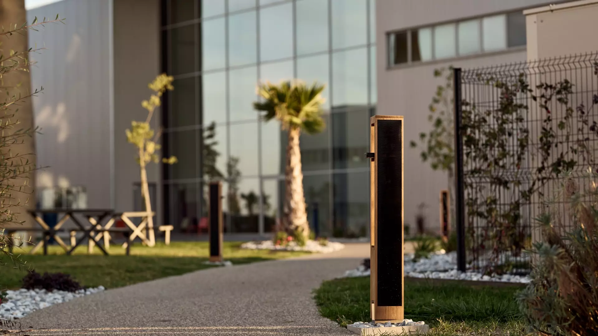 oko-solar-bollard-parking-area OKO solar bollard lights installed along a landscaped commercial walkway and parking area outside a modern building.