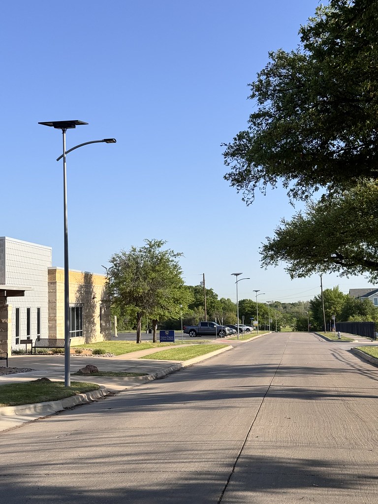 Solar-powered pathway bollard lighting installed along a sidewalk near a school and community services building, providing safe and reliable outdoor illumination.