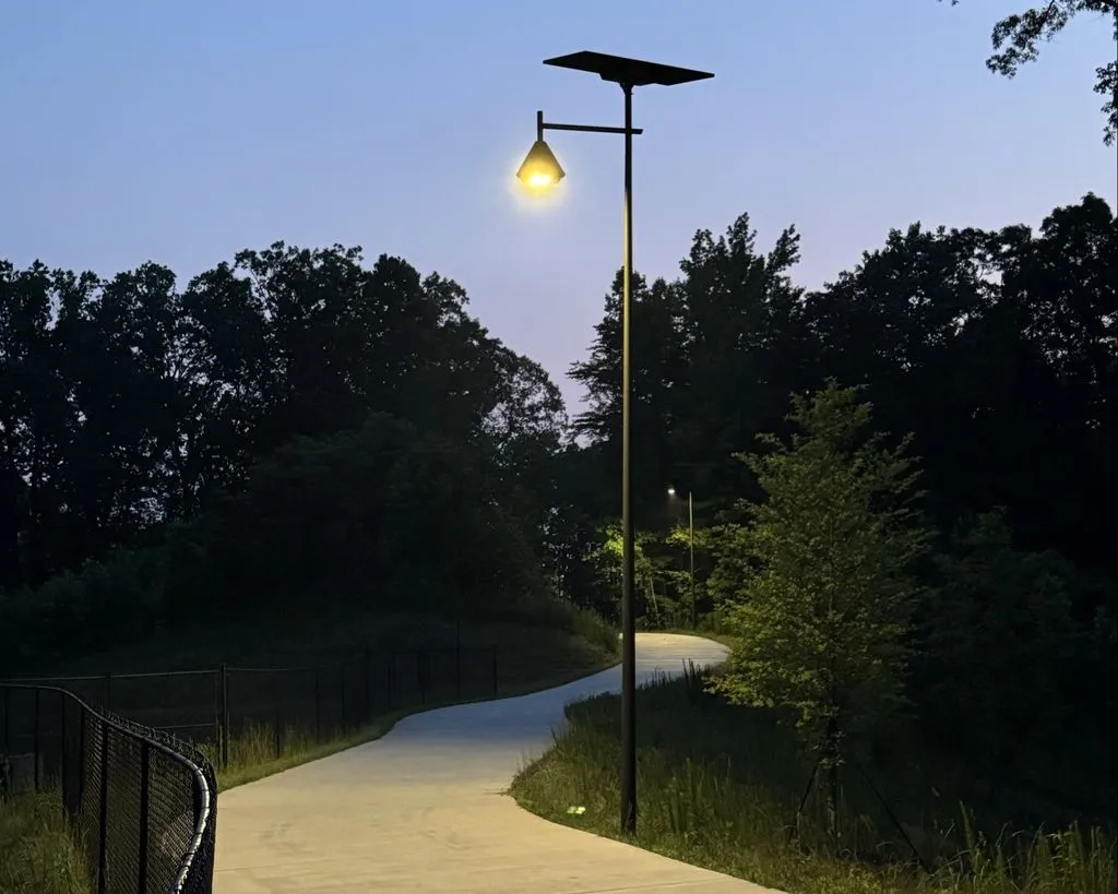 Fonroche solar streetlight illuminating a curved pedestrian pathway surrounded by trees and landscaping at dusk.