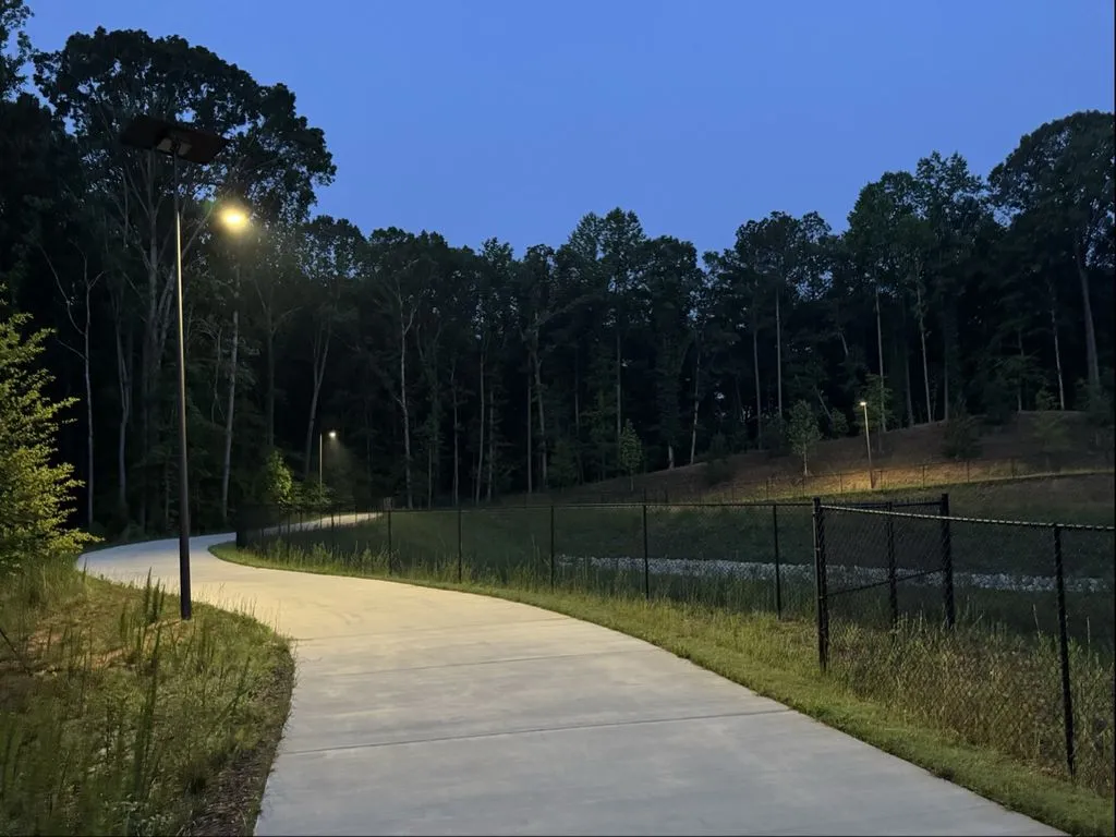 Fonroche solar streetlights illuminating a curved pedestrian pathway surrounded by mature trees and landscaped greenery at dusk.