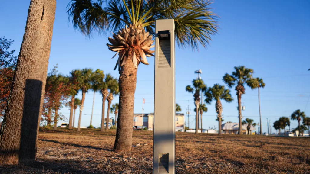 Solar pathway lighting bollard installed in a landscaped public space with palm trees.